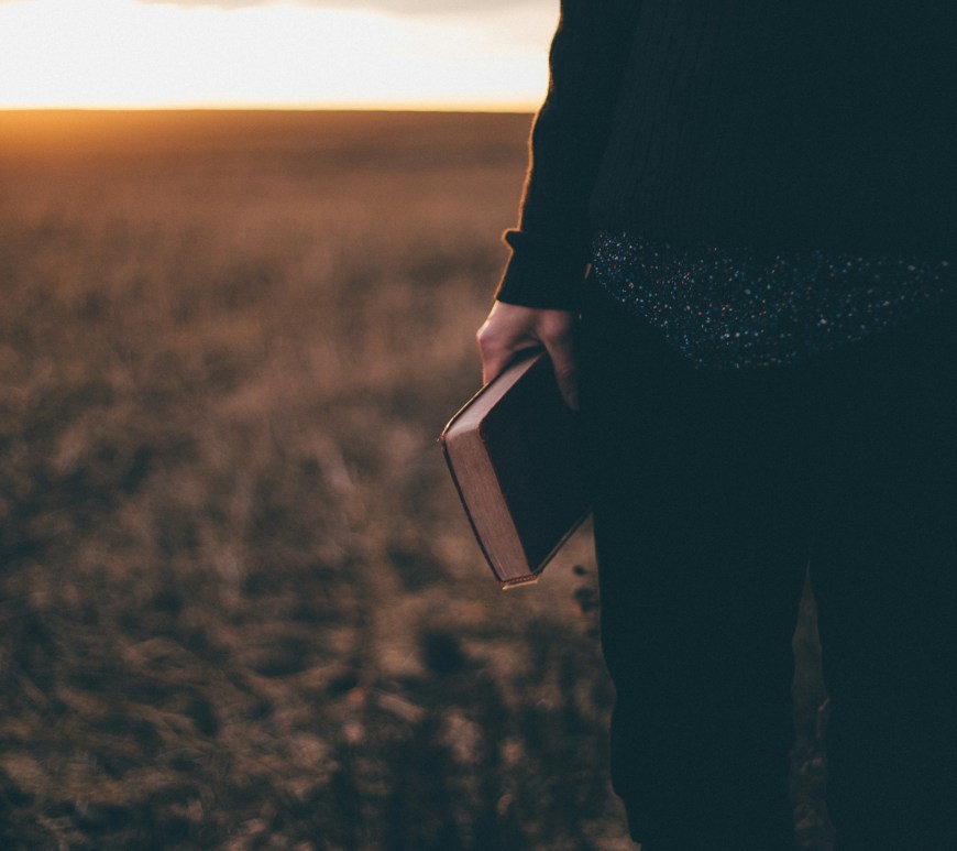A person in a field holding the Holy Bible.